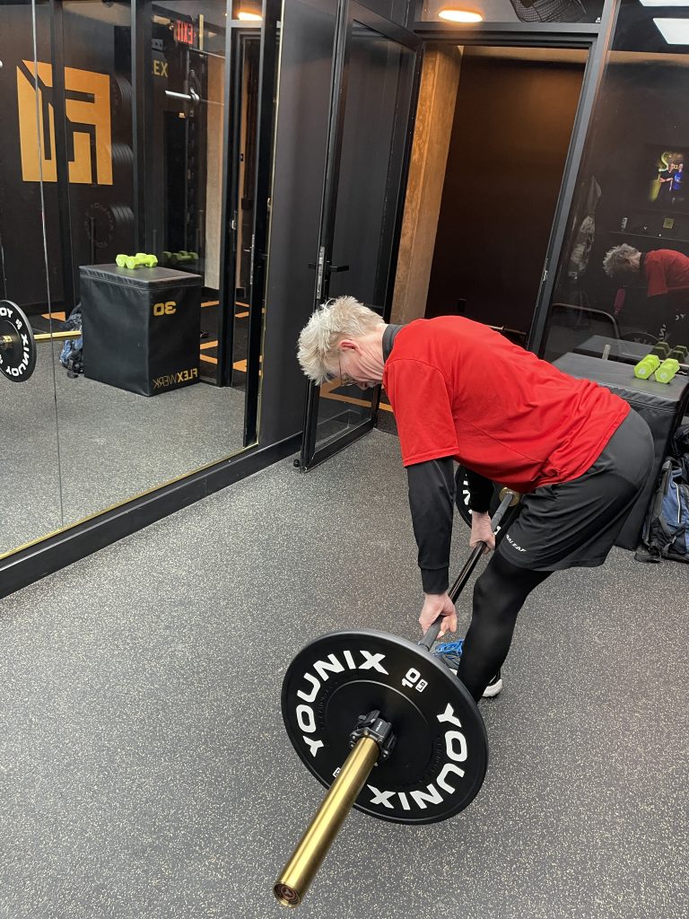 Senior client deadlifting with a barbell during personal training